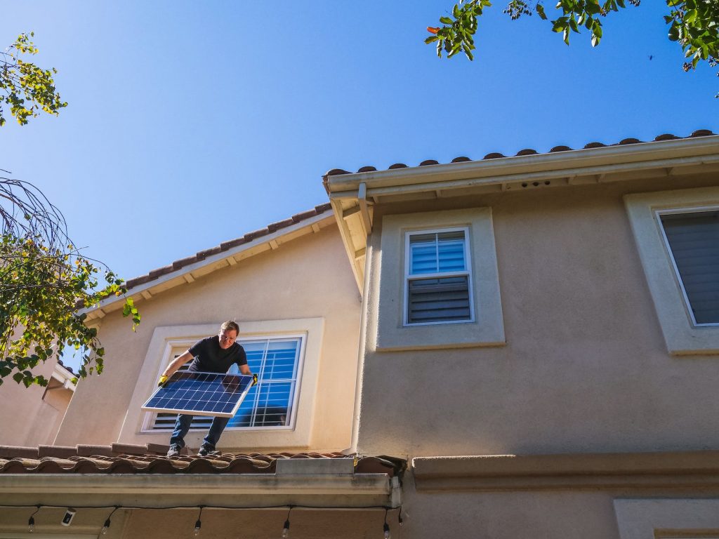 a man standing on the roof while holding a solar panel