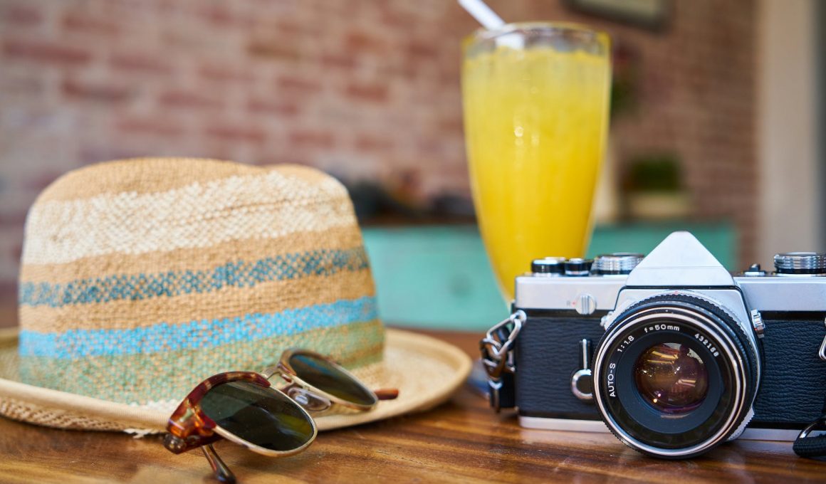 gray and black dslr camera beside sun hat and sunglasses